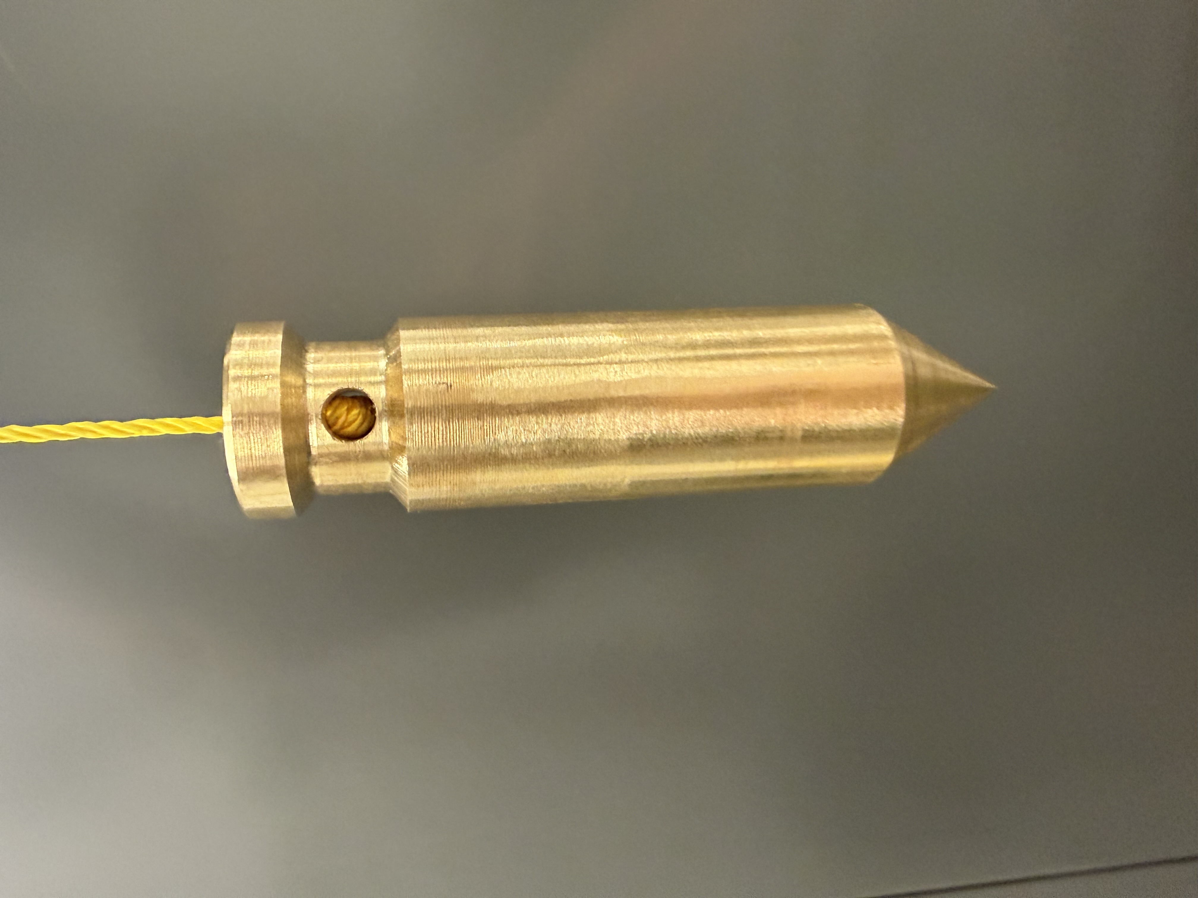 Gold-colored pointed machined component hanging from a yellow cord