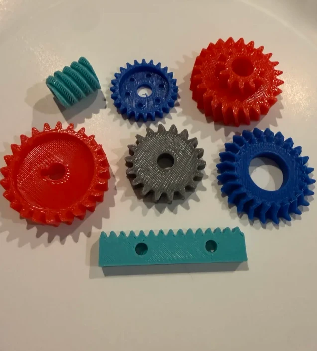 3D-printed parametric gears and a rack in red, blue, grey, and teal on a workshop floor